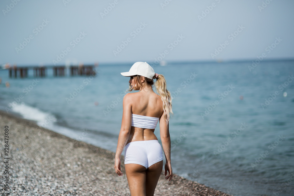 Back view of fitness girl walking along the beach