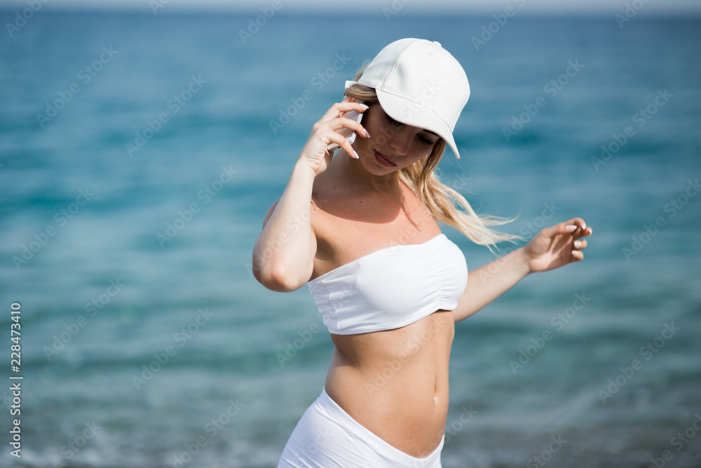 Young woman dressed in sportswear talking on the phone on the beach near the water Young woman dressed in sportswear talking on the phone on the beach near the water