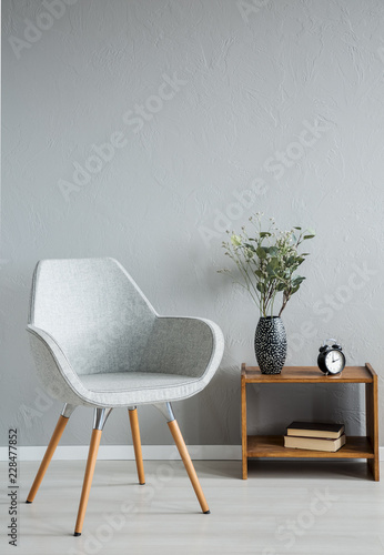Stylish grey chair next to cabinet with vase and flowers in modern office interior, real photo with copy space on the empty wall