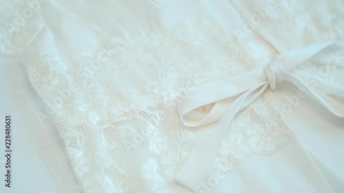 Tracking of wedding dress and dressing gown resting on bed on the wedding day. The white dress of the bride is resting on the bed on her wedding day. The white dressing gown with a white ribbon.