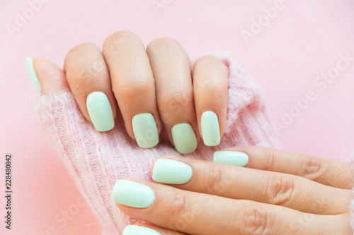 Tender hands with perfect blue manicure on trendy pastel pink background. Place for tex