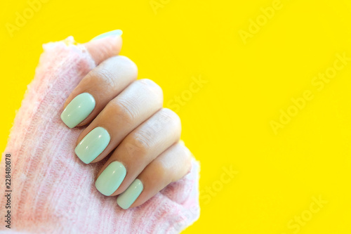 Tender hands with perfect blue manicure on trendy pastel yellow background. Place for tex