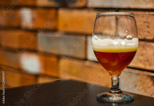 Close up on a glass of amber Pale Ale beer on wooden table in bar on brick wall background with copy space.