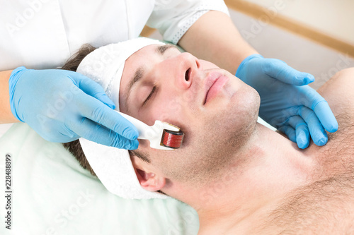 The man undergoes the procedure of medical micro needle therapy with a modern medical instrument derma roller. 