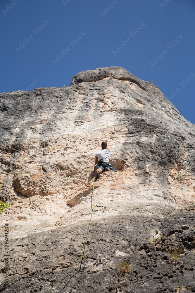 From below shot of male climber climbing mountain wall on amazing sunny day 