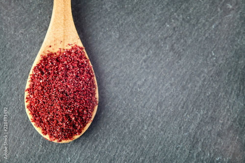 Ground sumac spice powder in wooden spoon. Top view with copy space