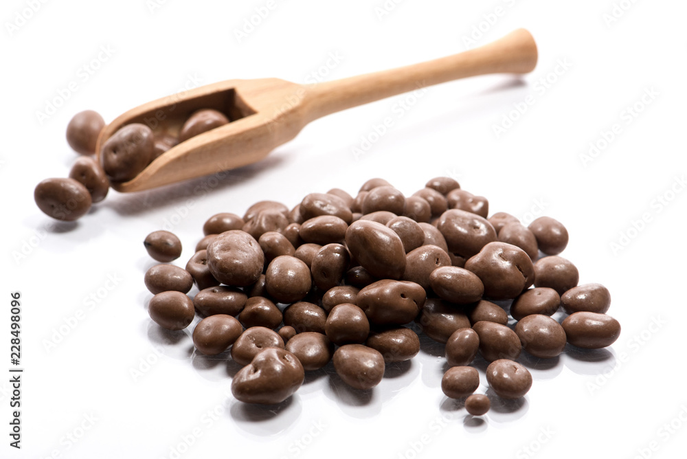 Fototapeta premium Close-up of pile dried, raw, chocolate raisins in a wooden spoon on white background