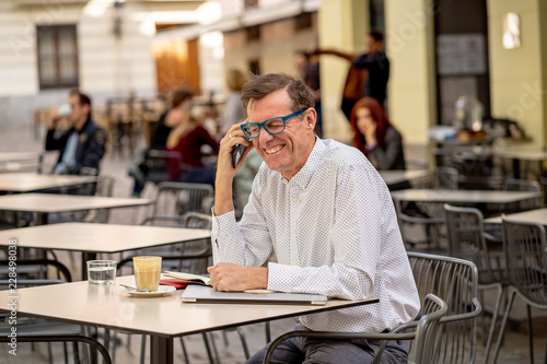 Smiling attractive stylish mature man using smart phone checking online sitting outside coffee shop