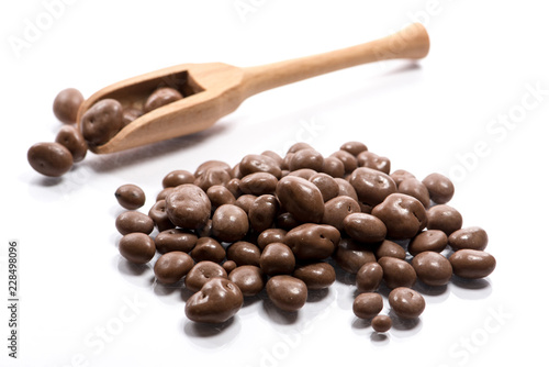 Close-up of pile dried, raw, chocolate raisins in a wooden spoon on white background