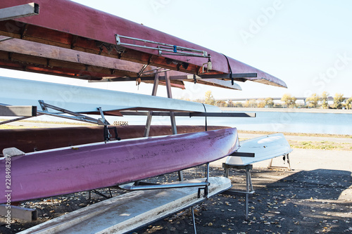 Old or spare kayaks are piled on top of each other by the lake.