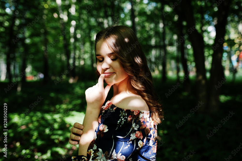 Fototapeta premium Portrait of a fabulous young girl in pretty dress with stylish curly hairstyle posing in the forest or park.