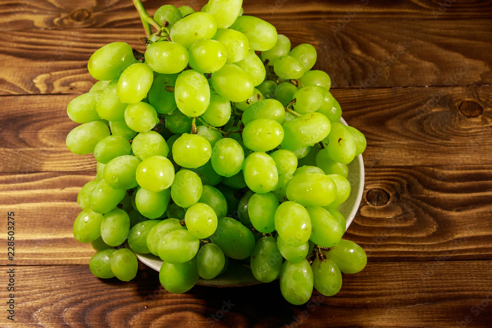 Tasty fresh white grape in a plate on wooden table Tasty fresh white grape in a plate on wooden table