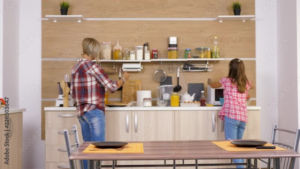 Mother and daughter at the kitchen bringing two big pizzas to the table Mother and daughter at the kitchen bringing two big pizzas to the table