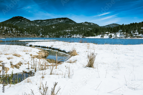 VIEW OF BRIGHT BLUE SKY WITH WHITE SNOW ON GROUND OF EVERGREEN LAKE IN LATE WINTER / COLORADO / USA