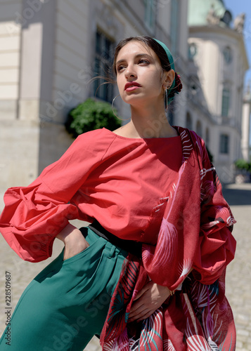 Young spanish woman in a red blouse and green pants. Fashion latin look. Woman walking in old town in Warsaw, Poland