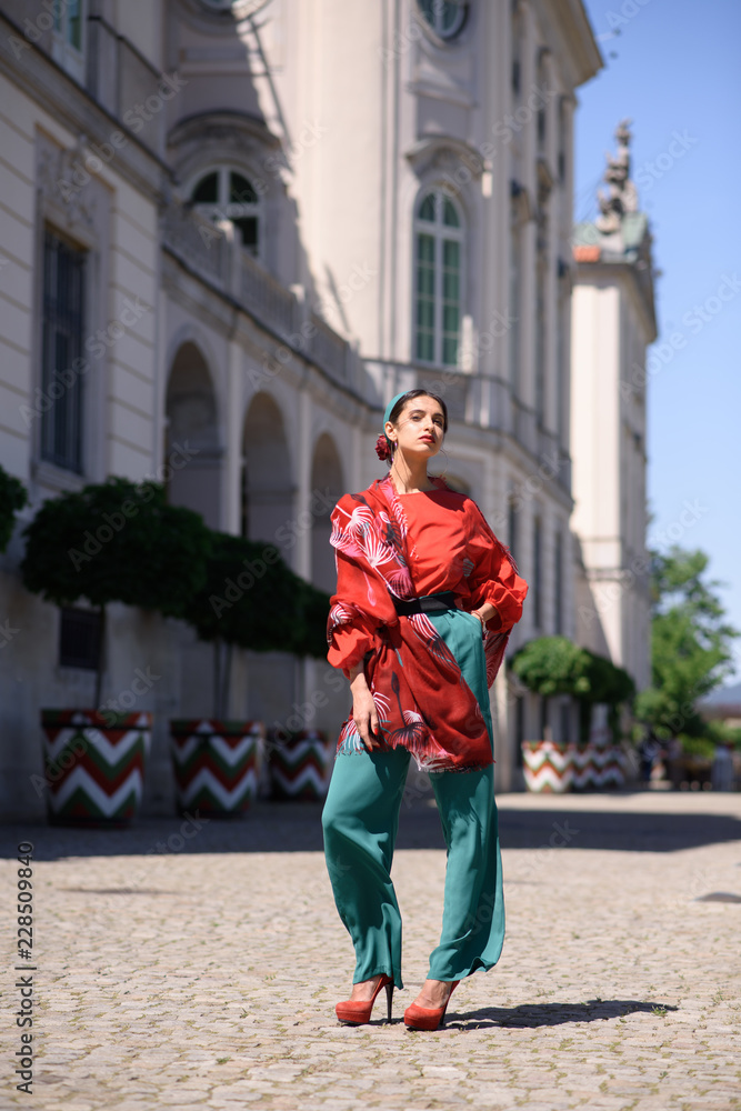 Young spanish woman in a red blouse and green pants. Fashion latin look. Woman walking in old town in Warsaw, Poland