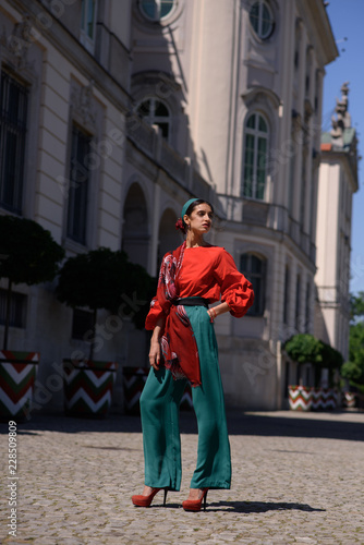 Young spanish woman in a red blouse and green pants. Fashion latin look. Woman walking in old town in Warsaw, Poland