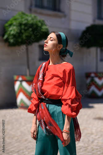 Young spanish woman in a red blouse and green pants. Fashion latin look. Woman walking in old town in Warsaw, Poland