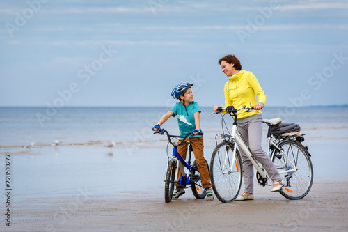 Young mother with her little son riding bicycles on beach