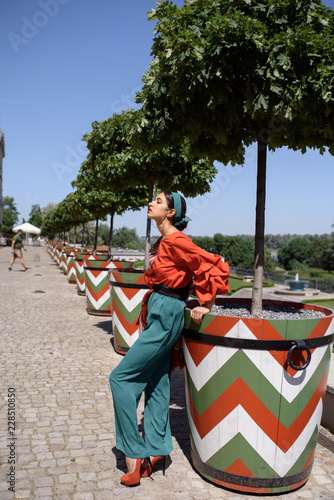 Young spanish woman in a red blouse and green pants. Fashion latin look. Woman walking in old town in Warsaw, Poland © Iulia