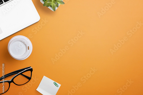Top view of orange office desk table with laptop, glasses, coffee, plant and sticky note. Flat lay