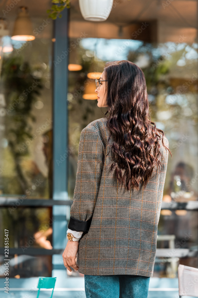 back view of beautiful woman in autumn outfit standing on street near cafe