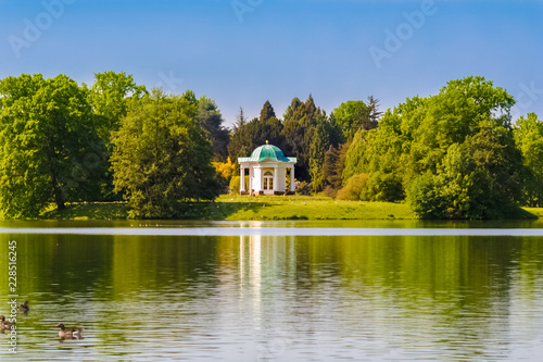 Beautiful scenery of Swan Island (Schwaneninsel) with its small white temple and ducks swimming on the lake (Aueteich) on a nice sunny day in the Karlsaue park in Kassel, Hesse, Germany. 