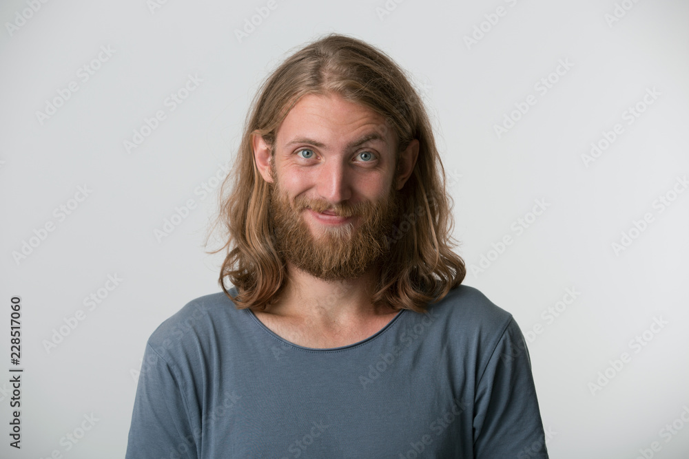 You really think so? Closeup photo of young man with a beard, blond hair to the shoulders and blue eyes looking with derisive, one corner of the lips is raised in a smile, over white background. You really think so? Closeup photo of young man with a beard, blond hair to the shoulders and blue eyes looking with derisive, one corner of the lips is raised in a smile, over white background.