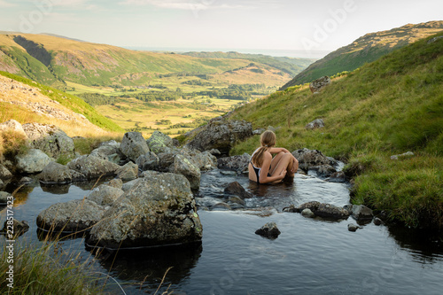 Girl sitting in Greendale Gill stream and looking at beautiful view of Wasdale valley in the Lake District National Park (UK) photo