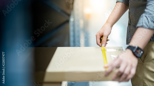 Male worker hand using tape measure for measuring dimension of product in cardboard box. Shopping lifestyle in warehouse concept
