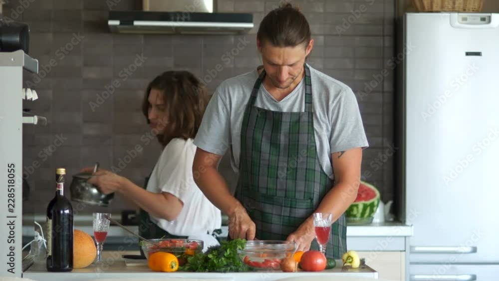 Husband and wife in the kitchen preparing dinner. He cuts the salad, she cooks the soup on the stove in the pan. Girl brings the pan, removes the lid, guy throws a piece of pepper there. Family humor Husband and wife in the kitchen preparing dinner. He cuts the salad, she cooks the soup on the stove in the pan. Girl brings the pan, removes the lid, guy throws a piece of pepper there. Family humor