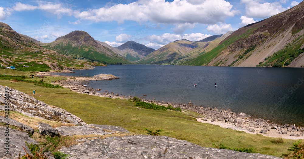 Stunning landscape view of Wast Water and fells in the Lake District National Park in the UK on a beautiful sunny day. Unidentified people paddle boarding on the lake