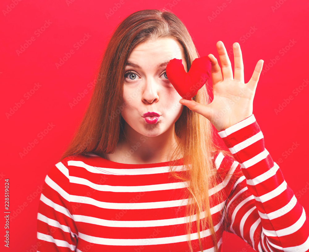 Happy young woman holding a heart cushion on a red background Happy young woman holding a heart cushion on a red background