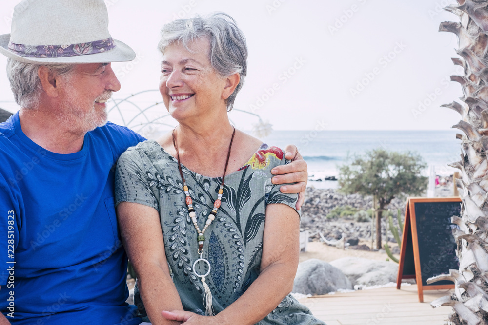 Happy senior couple laughing hugged on a summer day. concept of vacation, relaxation, rest. Blue sea in background. White clear sky and cheerful seniors