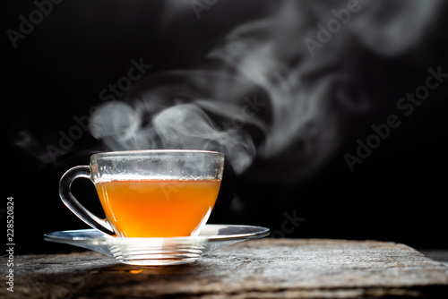 Hot tea in glass cup with steam and lemon .tea leaves and mint herb on wood background