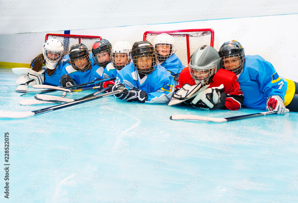 Fototapeta premium Joyful boys and girls laying on ice hockey rink