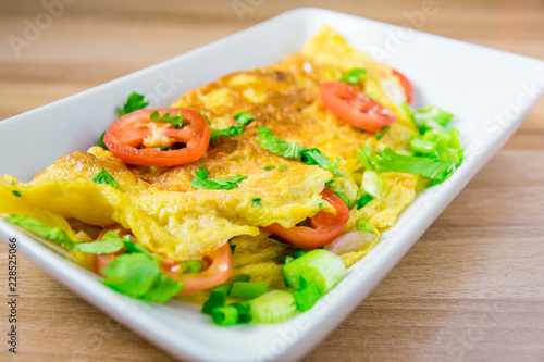 A photo of an omelette with cherry tomatoes, parsley. and grated cheese, shot from above on a rustic wooden texture with a place for text