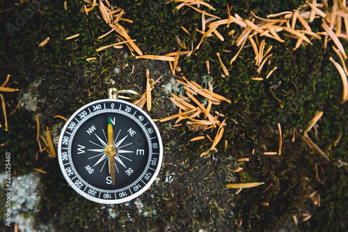 Magnetic compass with a black dial on a wild stone covered with green moss. The concept of finding the way and navigation