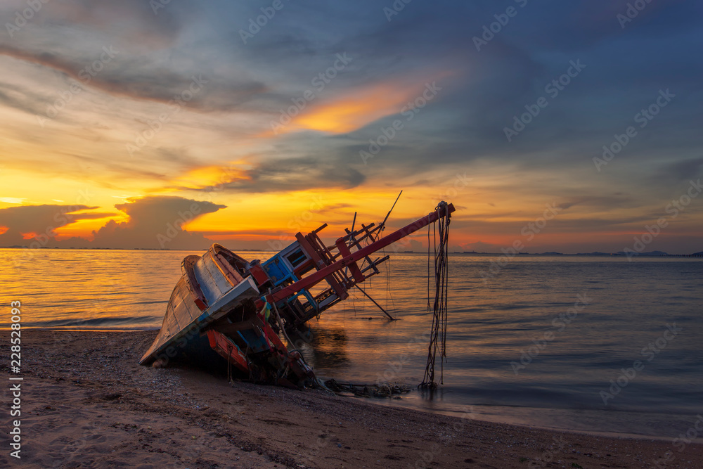 Beautiful sunset an old wooden is mouldy fishing boat on a pebble beach