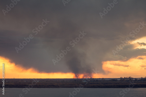 environmental pollution problem of fire on dry grass with smoke onthe horizon inflated by a strong wind during the sunset
