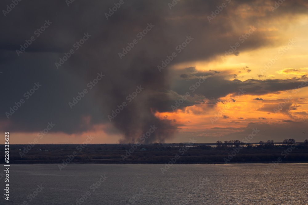environmental pollution problem of fire on dry grass with smoke onthe horizon inflated by a strong wind during the sunset