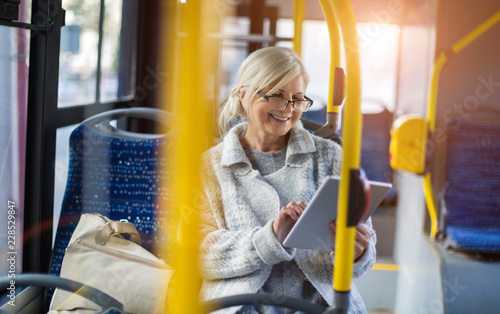 Senior woman using tablet, while riding public bus
