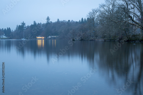 Still waters at dusk on lake windermere with orange lights. Lake District UK.