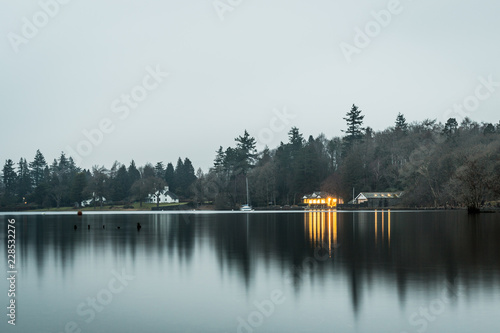 Still waters at dusk on lake windermere with orange lights. Lake District UK.