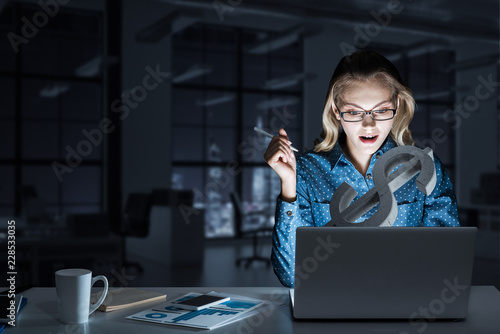 Attractive blonde wearing glasses in dark office using laptop. M