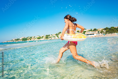 Young girl running into the sea with swimming tube