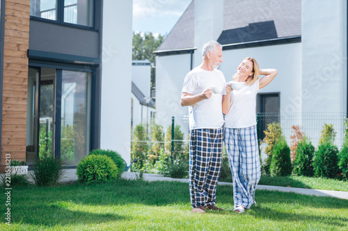 Pajama trousers. Beaming wife and husband wearing squared pajama trousers and house shoes standing on the grass