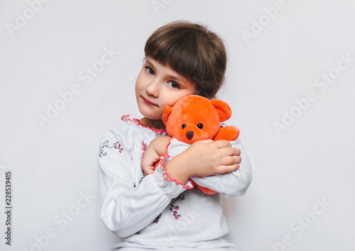 Fotografie A little girl is hugging a soft orange teddy bear on a white background