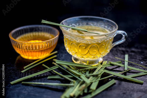 Close up of Iced lemon grass tea in a transparent cup on wooden surface with raw lemon grass green tea in a cup and sugar in a clay bowl with ice cubes in the cup and a piece of ginger and honey.