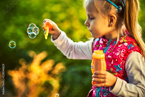 Pretty little girl and soap bubbles in autumn park